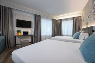 Een hotelkamer met twee bedden, een bureau met een computer, een televisie en een kunstwerk aan de muur.