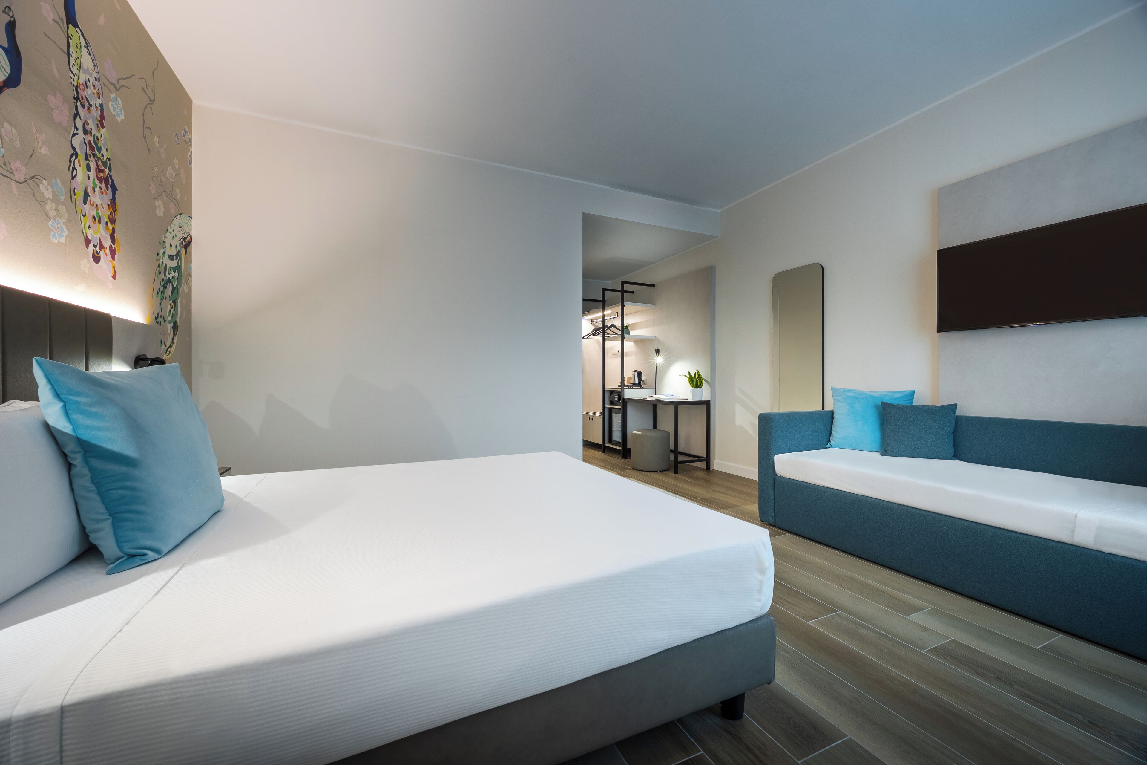 A modern hotel room with a large bed, a sofa, a desk, and a mirror.