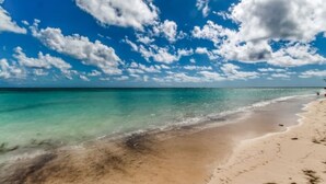 Een strand met helder turquoise water en een zandstrand, onder een blauwe lucht met verspreide wolken.