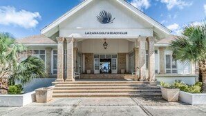 De ingang van Lacana Golf & Beach Club, met een goed zicht op de treden die naar de ingang leiden, palmbomen en een rustig zwembad.