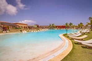 A swimming pool with lounge chairs, palm trees, and buildings with red-tiled roofs. - Fishing Lodge 2050 (Punta Cana)