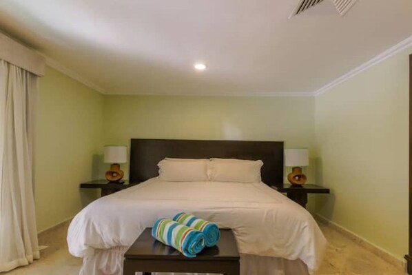 A hotel room with a bed, two bedside tables with lamps, and a small table with rolled towels.