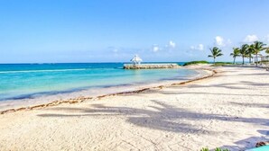 Una playa con aguas turquesas cristalinas, una orilla de arena blanca y algunas palmeras.