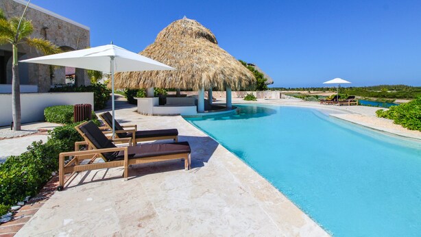 A pool area with lounge chairs and umbrellas, a thatched-roof structure, and a clear blue sky. - 2BDR Cap Cana Retreat @ GBL (Punta Cana)