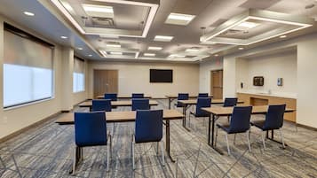 A conference room with a carpeted floor, rectangular tables, and blue chairs.