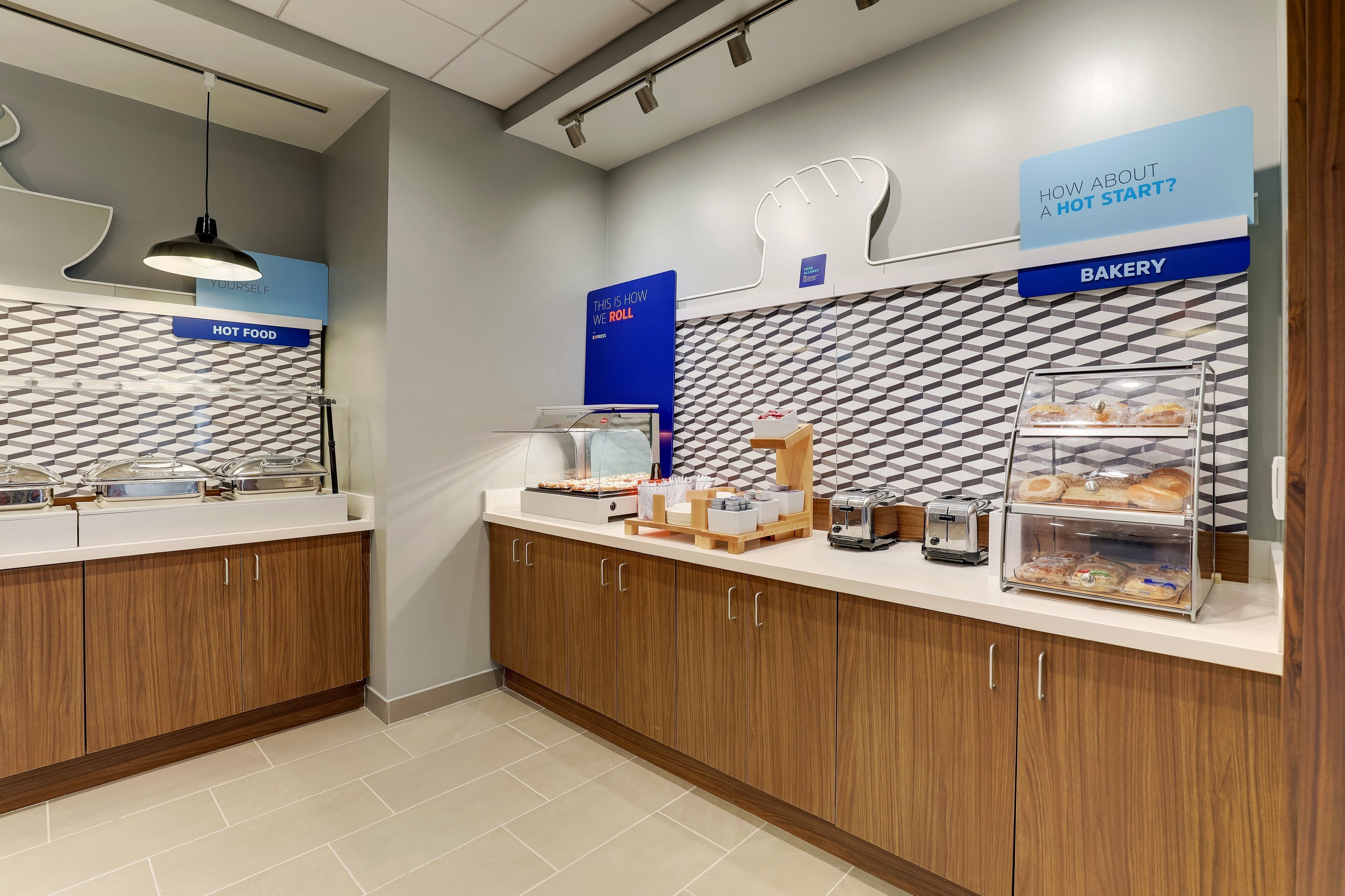 Un comptoir de boulangerie moderne, avec un mur orné d’un motif géométrique, une machine à café et une vitrine remplie de pâtisseries.