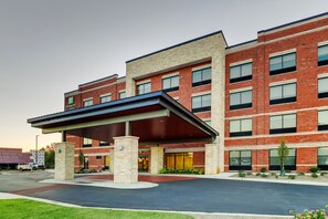 A modern hotel with a brick facade, a covered entrance, and a landscaped driveway.
