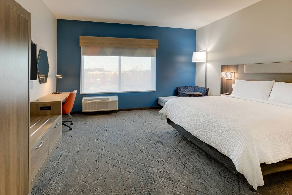 A hotel room with a bed, a desk, a chair, a window, and a wall-mounted TV.
