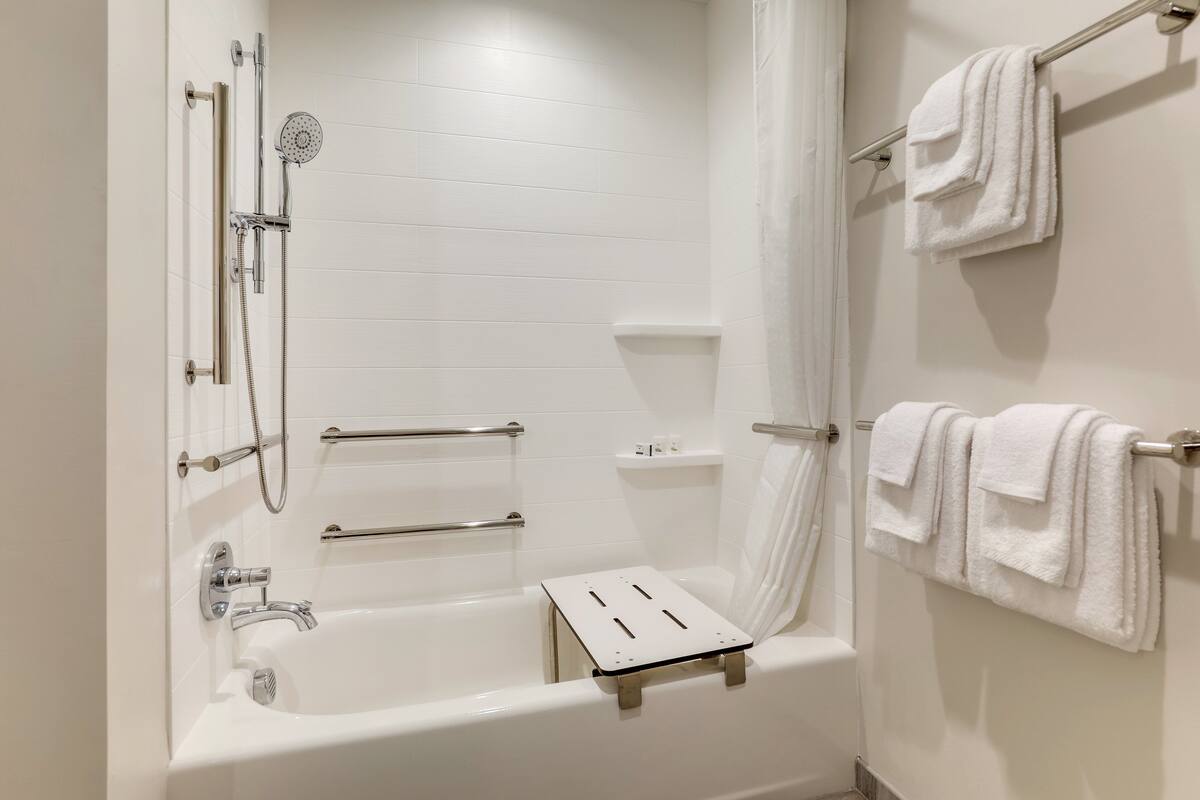 A modern bathroom with a bathtub, shower, and handrails.