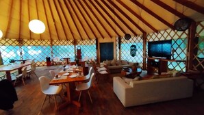 A spacious yurt with a wooden ceiling, a dining area with a table and chairs, a sofa, and a television. - Magma Lodge Pucon (Pucón)