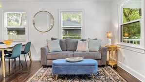 Un salon avec un canapé gris, un pouf bleu et un miroir rond accroché au mur.