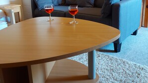 A cozy living room with a wooden coffee table, two glasses of red wine, a grey sofa with blue cushions, and a white brick wall. - Vacation at the Uhlenhoff Apartment Ewiges Meer (Ihlow)