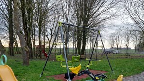 A playground with swings, a slide, and a toy tractor. - Vacation at the Uhlenhoff Apartment Ewiges Meer (Ihlow)