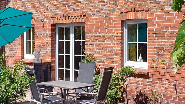 A brick building with a patio area featuring a table and chairs, a green umbrella, and a sign reading "E. C. Hoffmann". - Vacation at the Uhlenhoff Apartment Ewiges Meer (Ihlow)