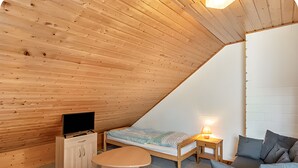 A cozy attic bedroom with a wooden sloped ceiling, a bed, a sofa, a TV, and a small table. - Vacation at the Uhlenhoff Apartment Ewiges Meer (Ihlow)