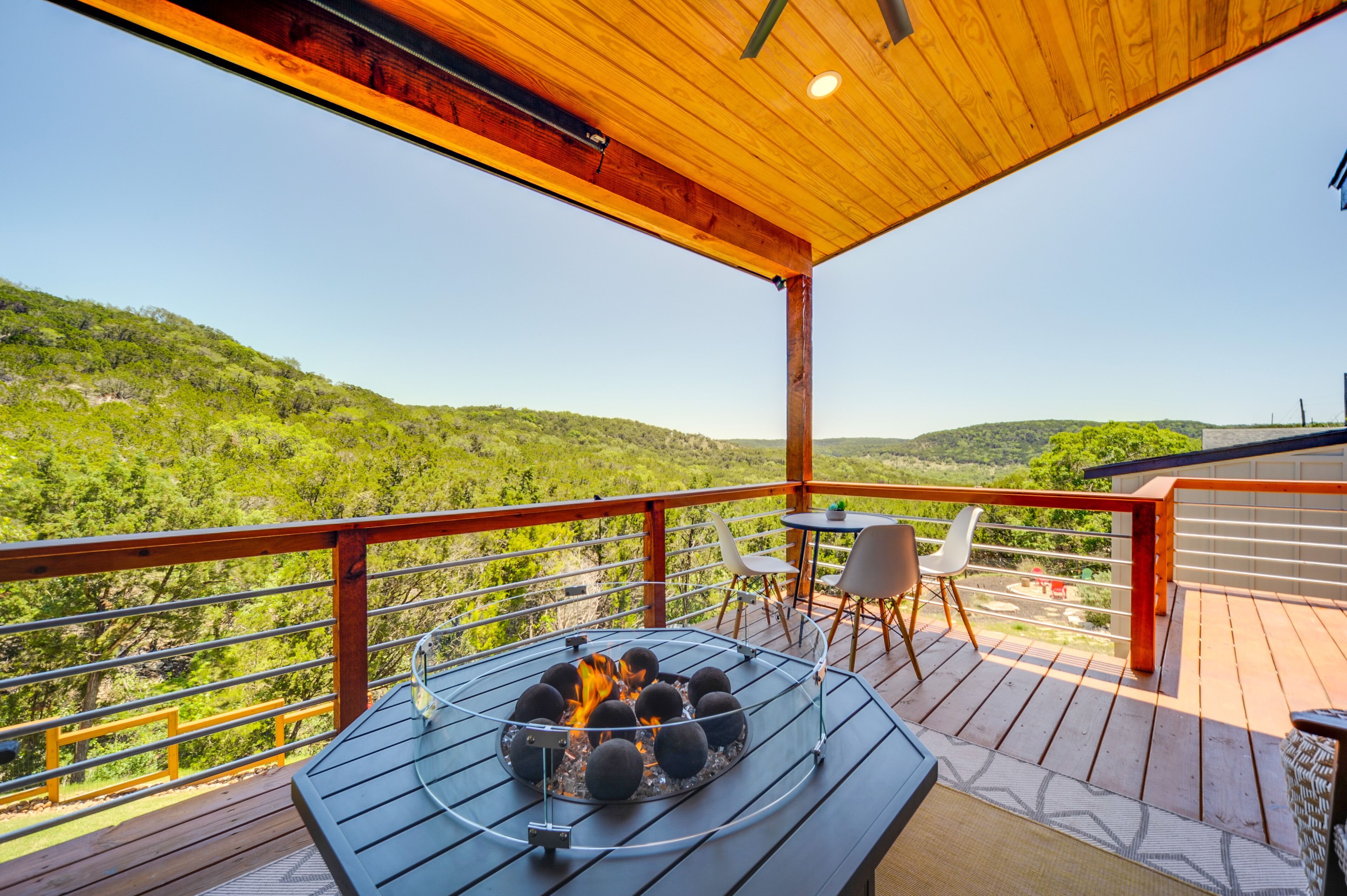 A wooden deck with a fire pit, outdoor seating, and a scenic view of a forested hillside.