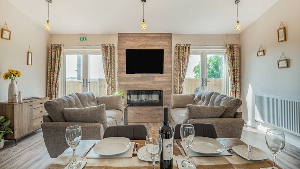 A dining area with a table set for four, a fireplace, and a television mounted on the wall. - West End Farm Lodge Alabaster (Ruardean, Forest of Dean)
