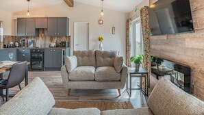 A modern living room with a sofa, a dining table, and a kitchen in the background. - West End Farm Lodge Alabaster (Ruardean, Forest of Dean)