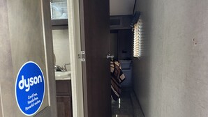 Een smalle gang met een Dyson logo aan de linkerkant, die leidt naar een badkamer met een handdoek aan de deur.