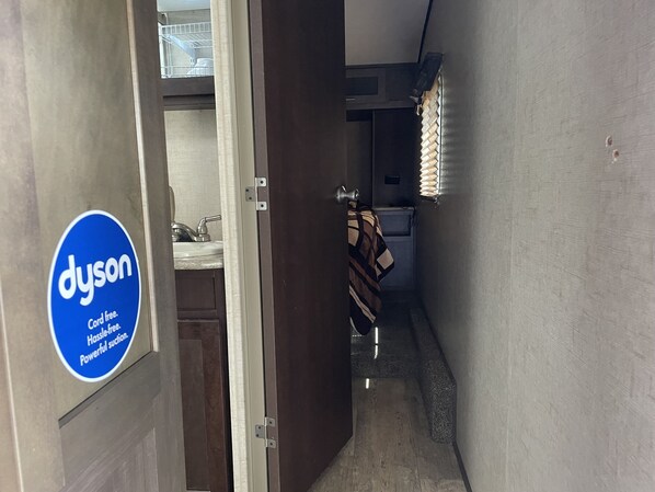 Un pasillo estrecho con el logotipo de Dyson a la izquierda, que conduce a un baño con una toalla colgada en la puerta.