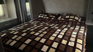Een bed met een geruit laken, een raam met zonwering en een deur met een knop.