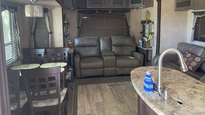 Een compact RV-interieur met een kitchenette, een zithoek met een bank en een eettafel.