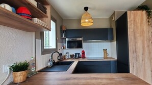 A compact kitchen with a wooden countertop, a built-in microwave, and a hanging light fixture. - Lumineux appartement avec vue sur mer (Saint-Raphaël)