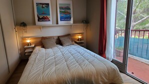 A bedroom with a bed, two nightstands with lamps, a window with a view of greenery, and two framed pictures on the wall. - Lumineux appartement avec vue sur mer (Saint-Raphaël)