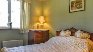 Une chambre à coucher avec un lit, une commode, une lampe et une fenêtre avec des rideaux.