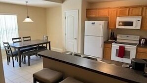 A kitchen with a central island, a dining area with chairs, and wooden cabinets. - Lovely 3-Bedroom Pool With Spa (Clermont)