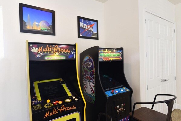 Two arcade machines labeled 'Multi Arcade Video Game' in a room with white walls, a door, and a framed picture of a cityscape.