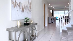 A modern living room with a large abstract painting, a console table with decorative items, and a staircase leading to another area.