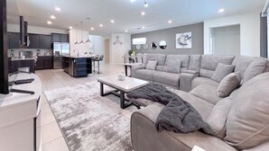 A modern living room with a grey sofa, a coffee table, and a kitchen area in the background.