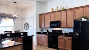 Une cuisine avec des meubles de rangement en bois, un réfrigérateur noir, un four à micro-ondes et une cuisinière.