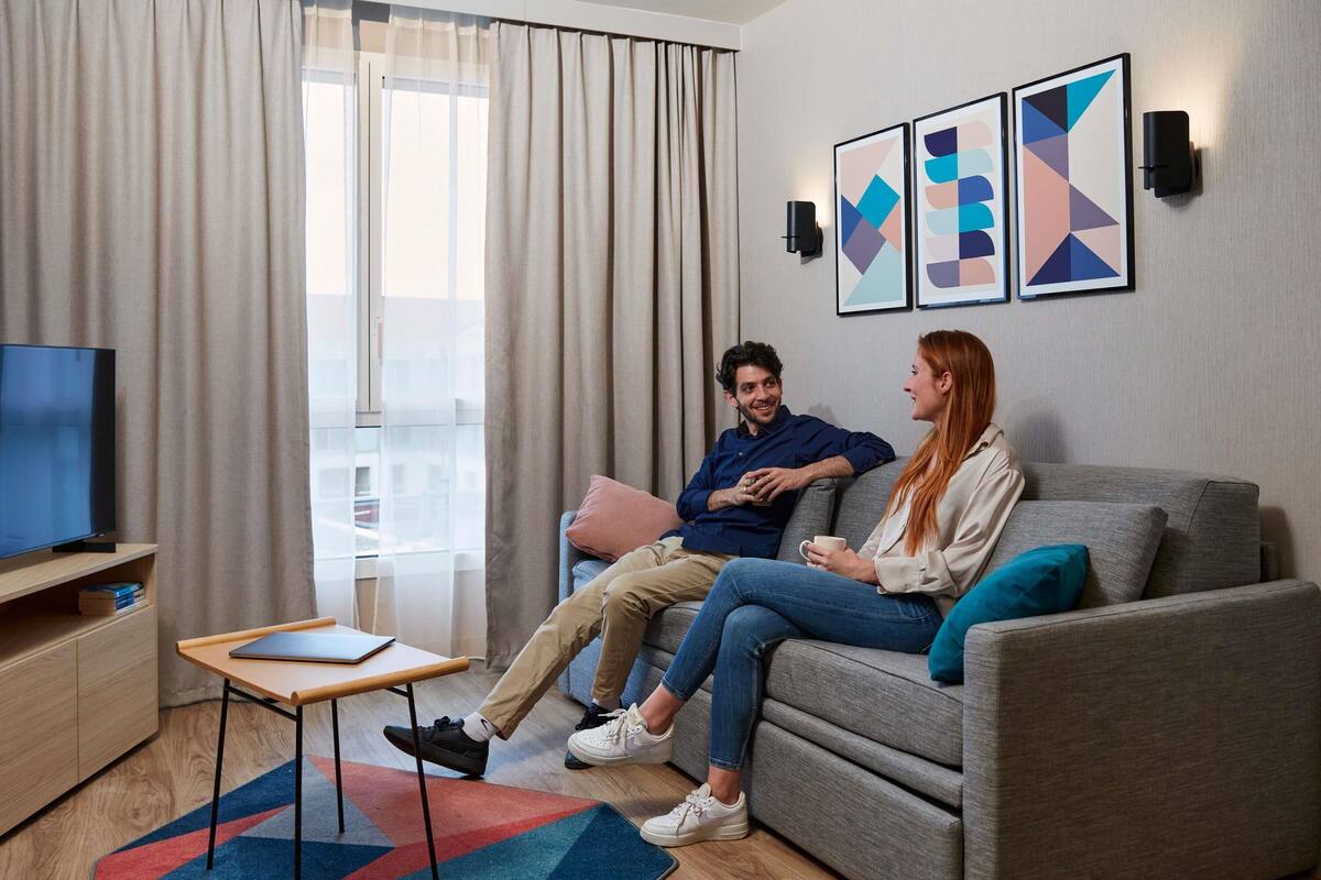 A modern living room with a sofa, a coffee table, a TV, and a window with curtains.