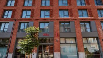 A multi-story building with a red brick facade, large windows, and a visible entrance with a sign.