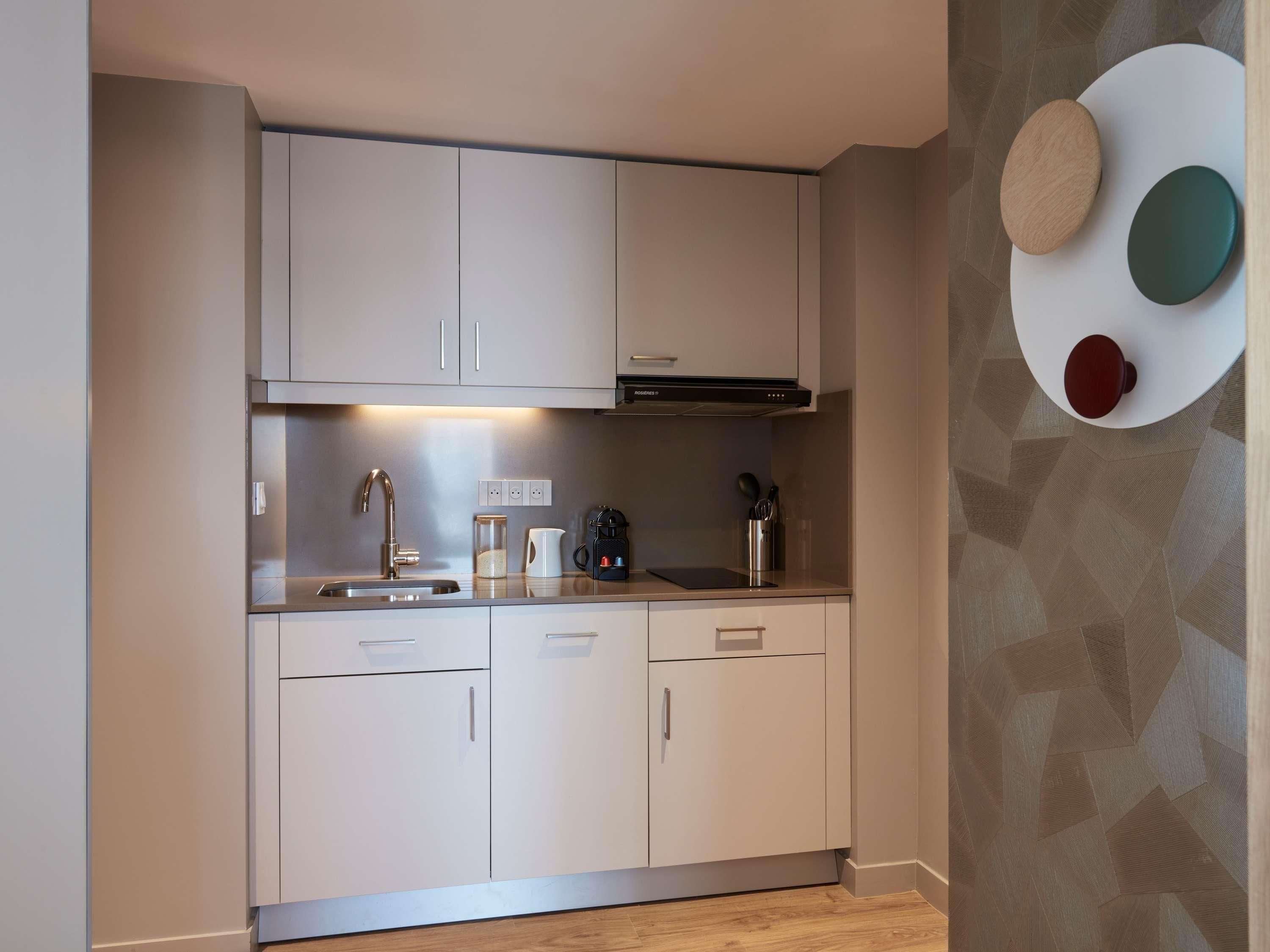 Une cuisine moderne avec des meubles blancs, un évier en acier inoxydable et une machine à café.