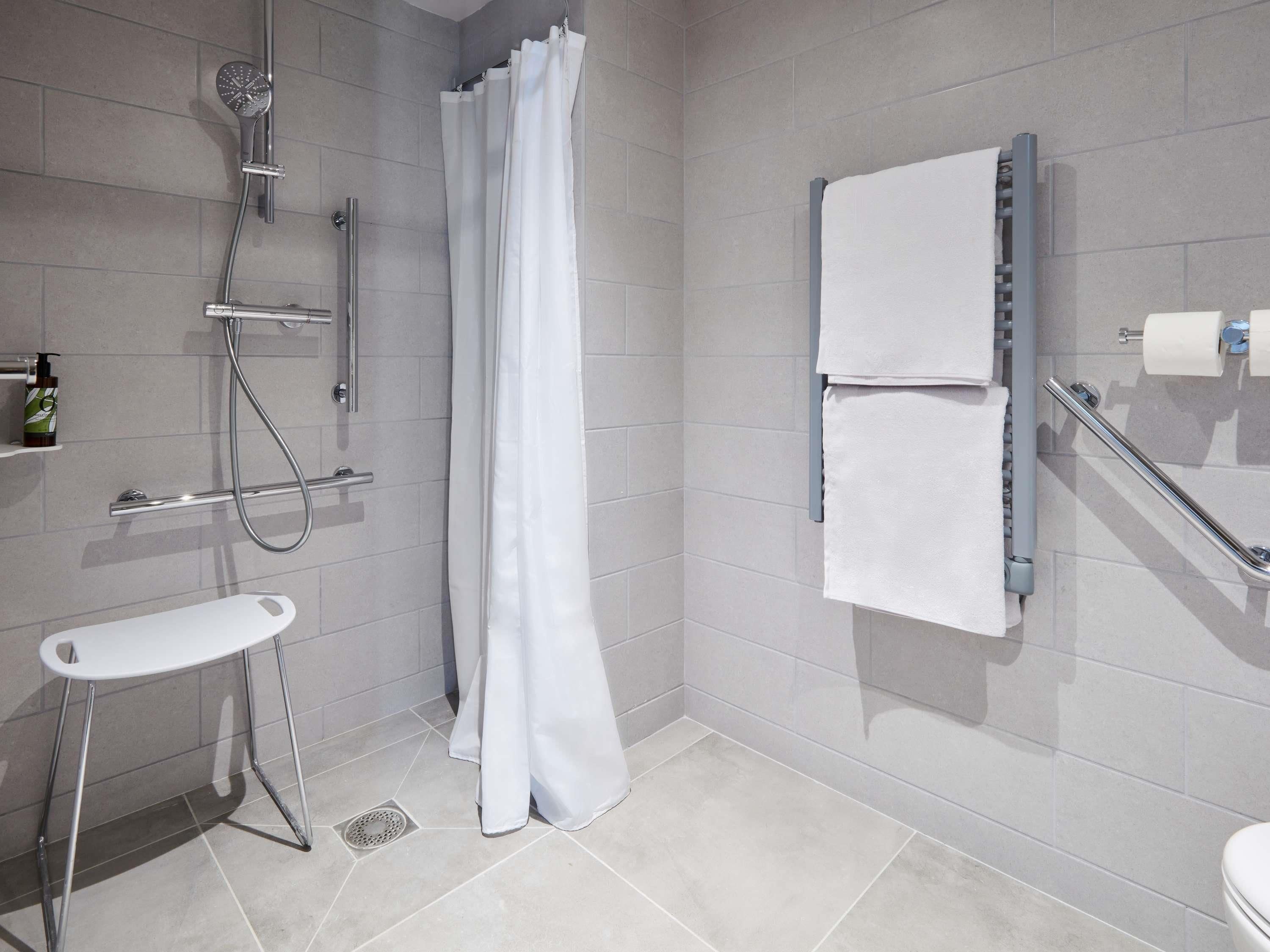 A modern bathroom with a shower, toilet, and a small stool.