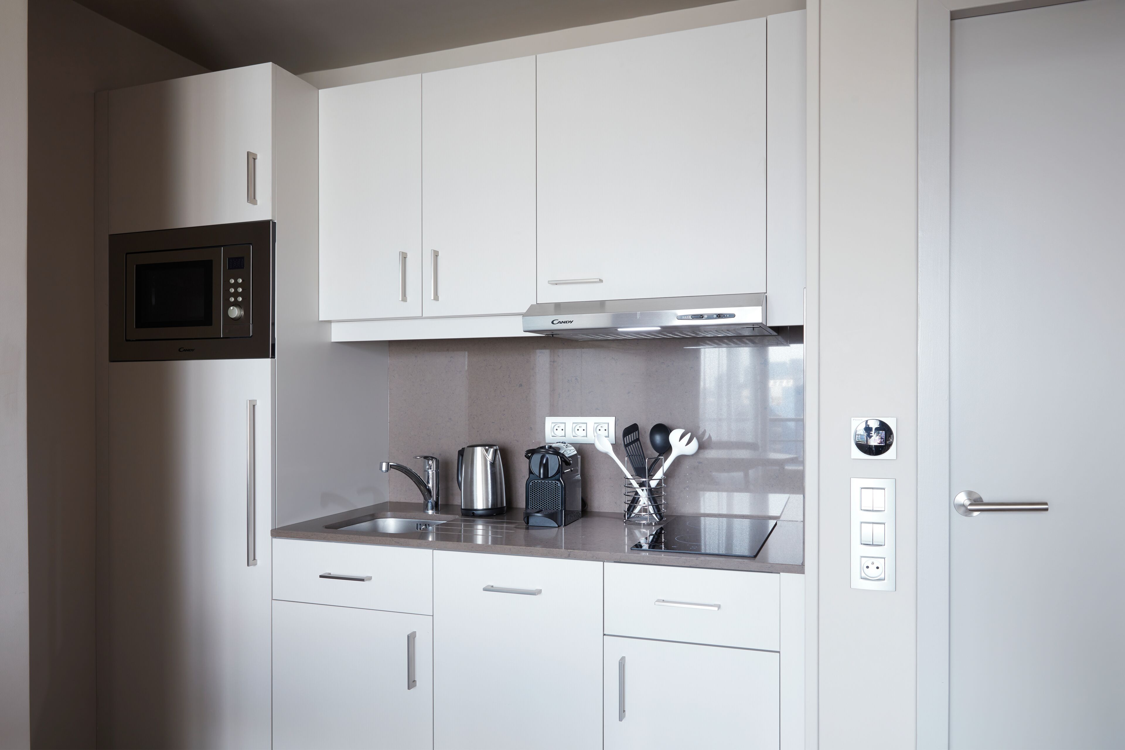 A modern kitchen with white cabinets, a microwave, a kettle, and a coffee maker.