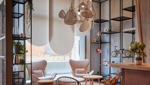 Una sala de estar moderna con un conjunto de sofá, una mesa de centro y una zona de comedor con sillas. Hay estanterías con libros y objetos decorativos, y un ventanal que proporciona luz natural.