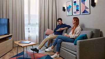 A modern living room with a sofa, a coffee table, a TV, and a window with curtains.