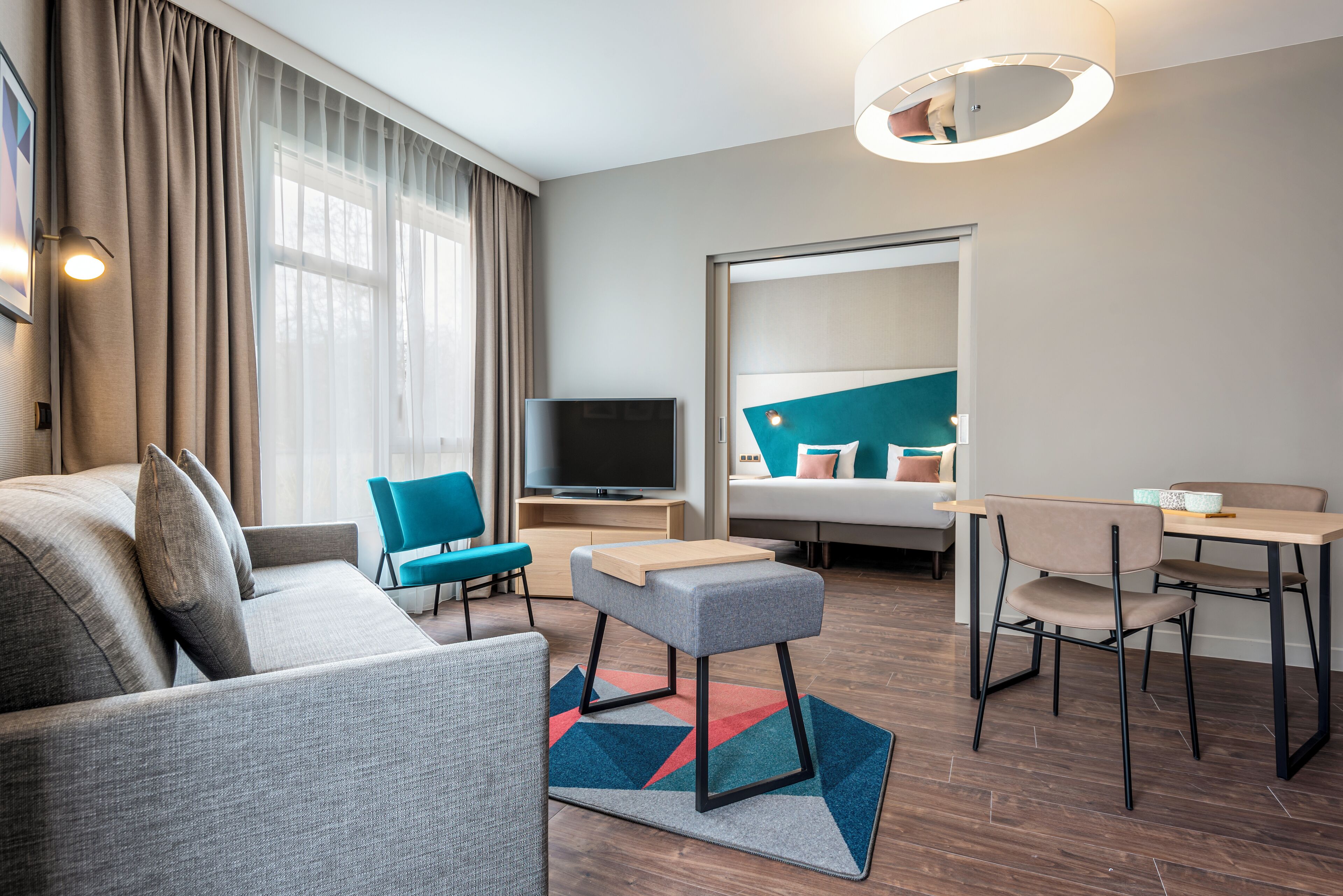Ein modernes Hotelzimmer mit einer Couch, einem kleinen Tisch, einem Sessel, einem Fernseher und einem Bett mit Kopfteil.