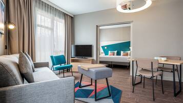 Ein modernes Hotelzimmer mit einer Couch, einem kleinen Tisch, einem Sessel, einem Fernseher und einem Bett mit Kopfteil.