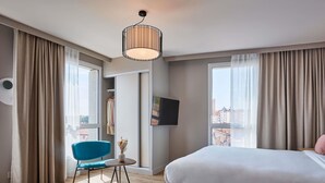 Una habitación de hotel moderna con una cama grande, una silla azul, una mesita y un televisor en la pared.