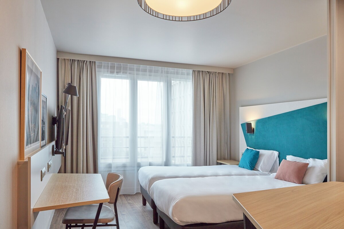 A hotel room with two beds, a desk, and a chair.