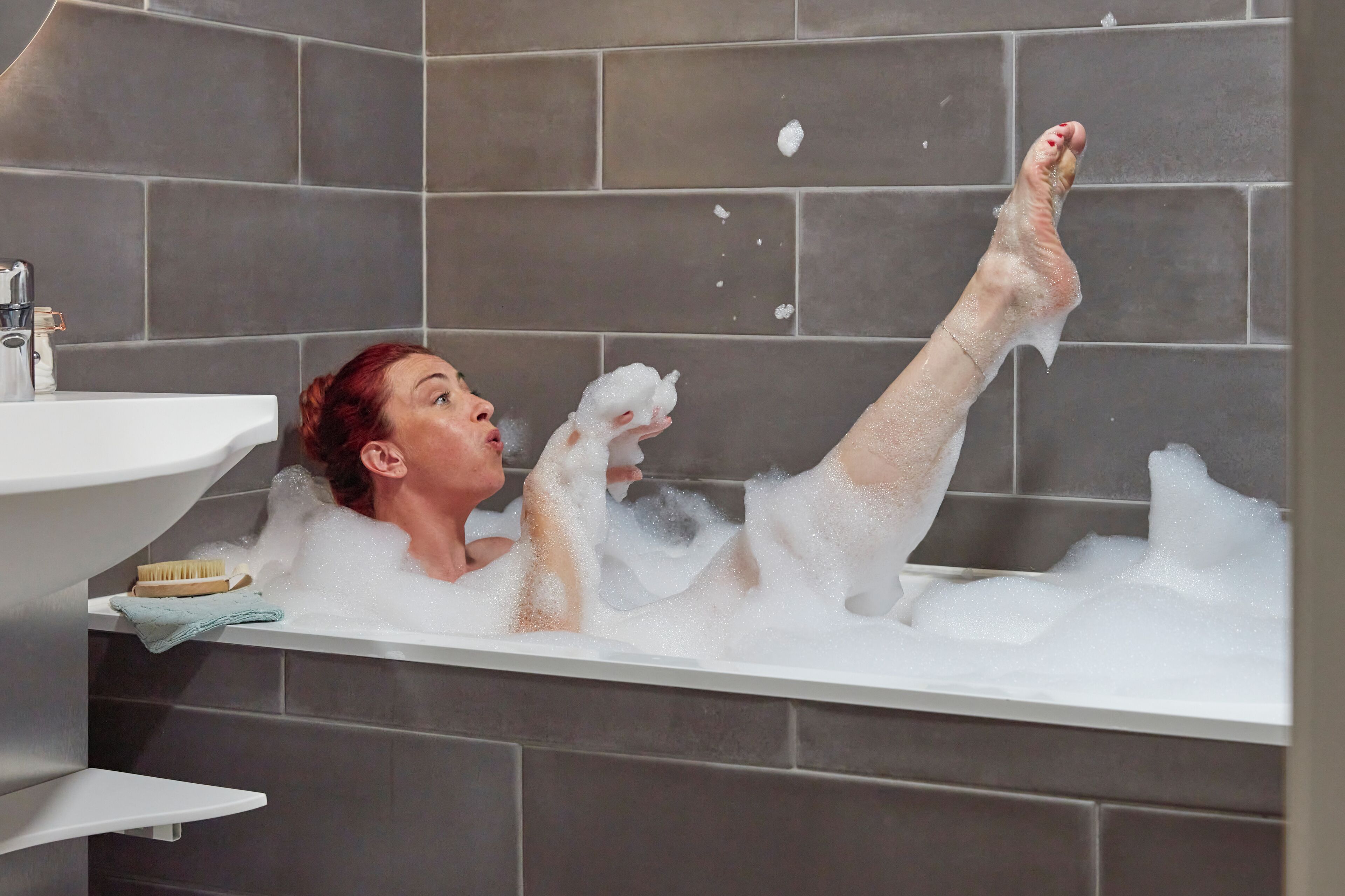 A person in a bathtub with bubbles, a sink, and a towel rack.