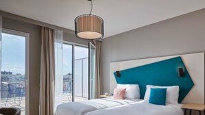 Una habitación de hotel moderna con dos camas, un ventanal con vistas y una lámpara en el techo.