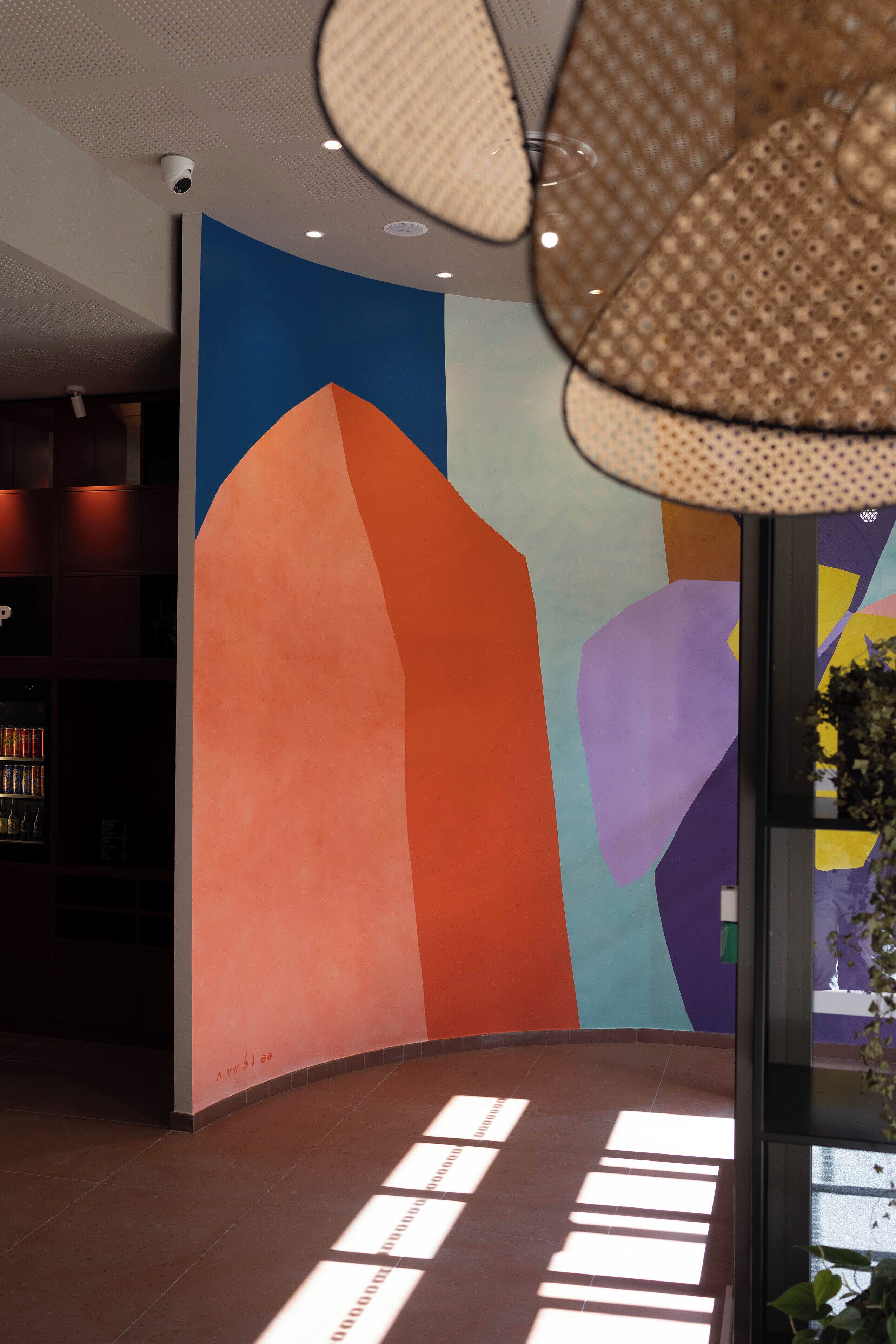 Un interior moderno con un gran mural abstracto, un techo con iluminación empotrada y un vidrio con vistas al exterior.