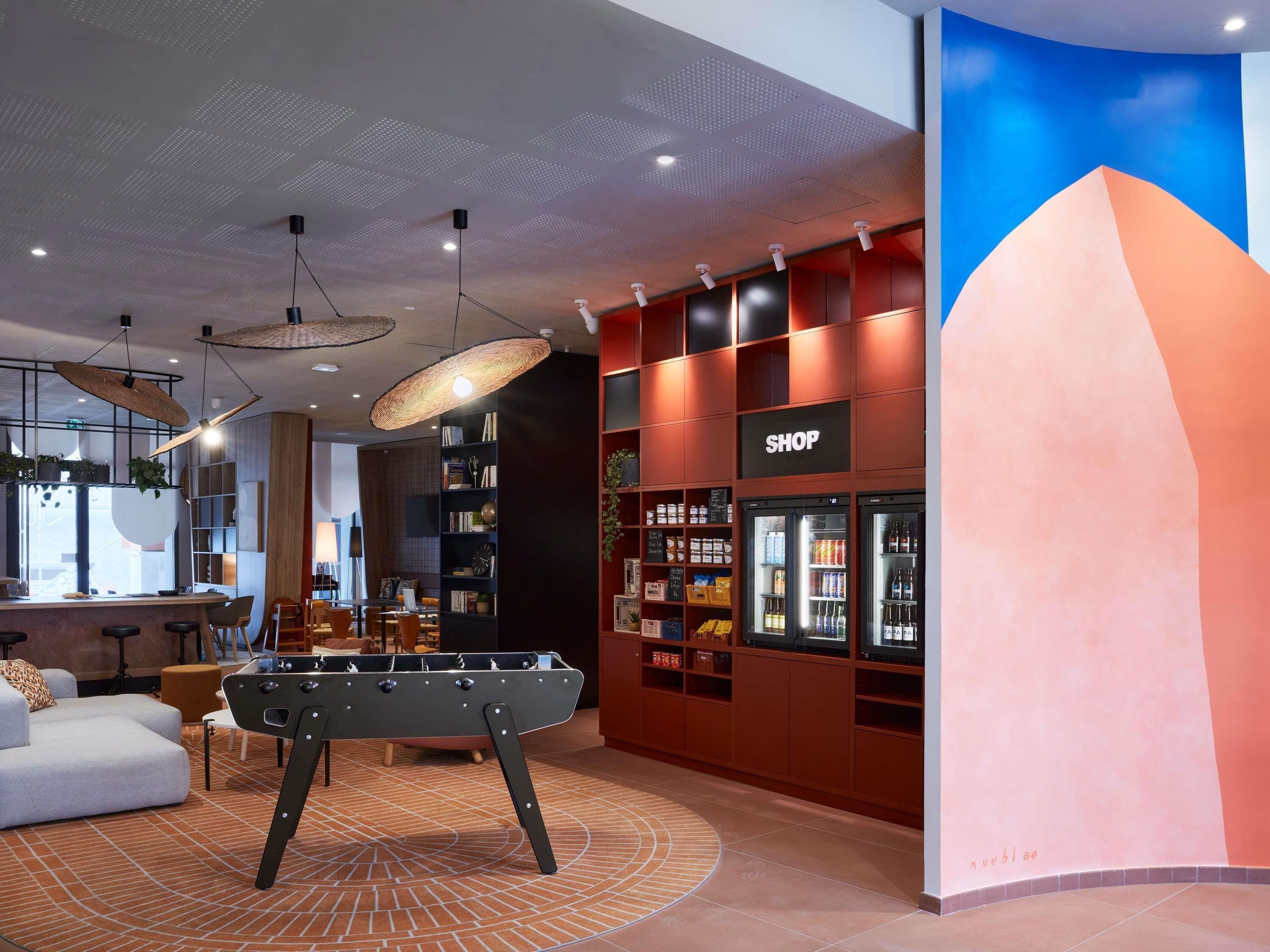 A modern interior with a foosball table, a bar area, and a shop with refrigerated beverages.