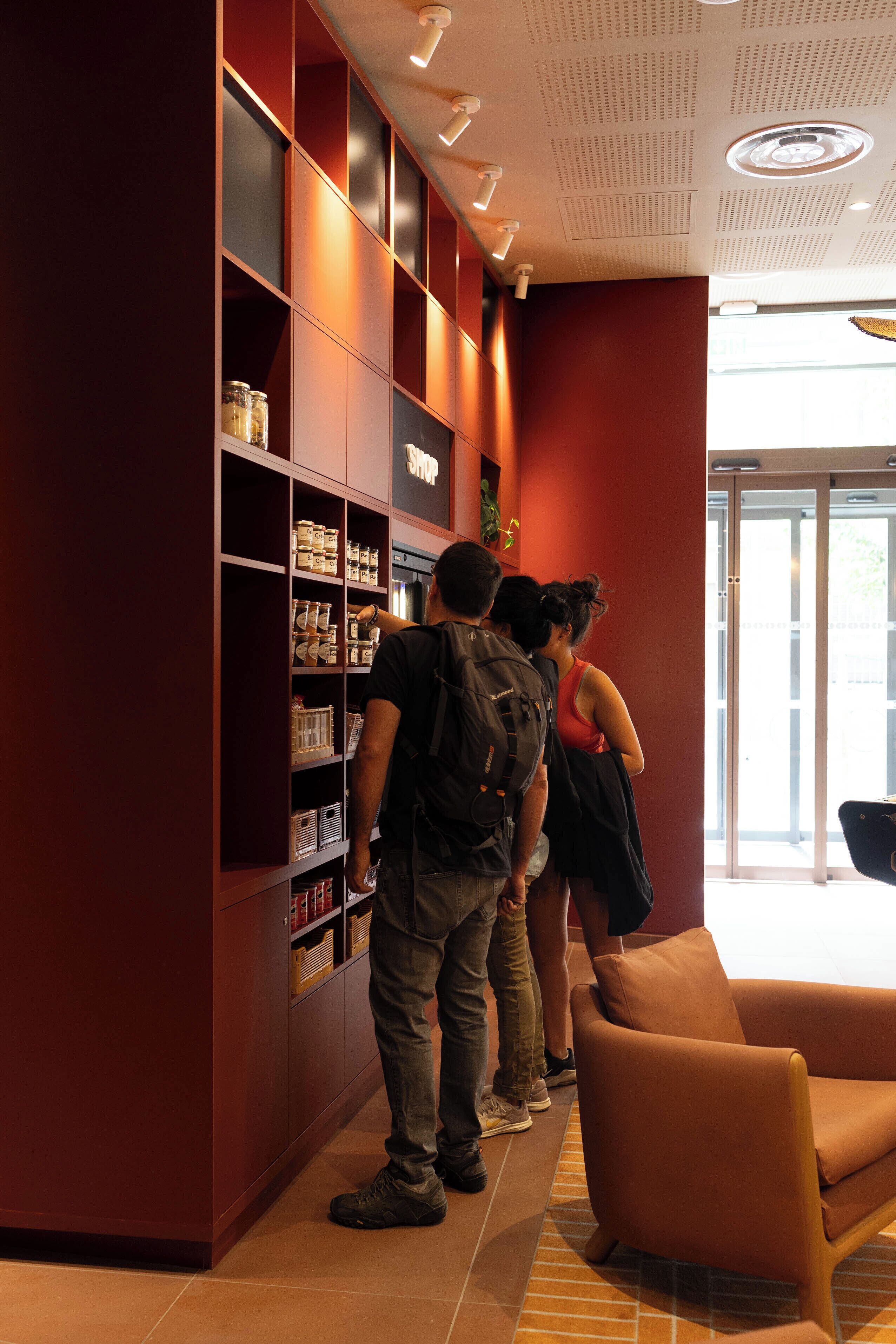 Een groep mensen staat voor een boekenkast in een kamer met een rode muur en een groot raam.